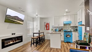 A modern kitchen with white cabinets, a blue stove, and a flat-screen TV mounted on the wall. - Dapper Duo 5BR/5BA in 2 Houses w/Fenced Yards, AC, WD, Fast Wi-Fi, 7 Smart TVs (Flagstaff)