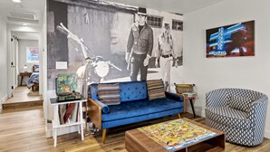 A living room with a blue sofa, a patterned armchair, a coffee table with a puzzle, a bookshelf with books and a vintage radio, and a large black and white mural on the wall. - Dapper Duo 5BR/5BA in 2 Houses w/Fenced Yards, AC, WD, Fast Wi-Fi, 7 Smart TVs (Flagstaff)