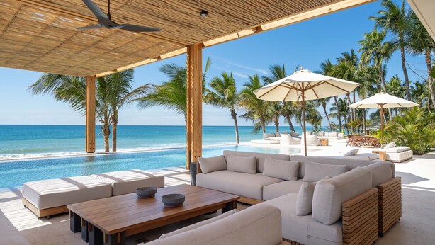 Een strandlounge met een zwembad, terras en palmbomen.