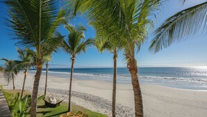 Een strand met palmbomen, een hangmat en een tafel met stoelen.