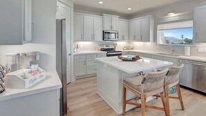 Una cocina moderna con armarios blancos, una isla central y un comedor con sillas de mimbre.