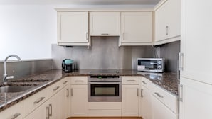 Een compacte keuken met witte kastjes, een roestvrijstalen oven, een magnetron en een koffiezetapparaat.