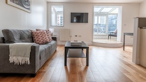 Een moderne woonkamer met een grijze bank, een salontafel en een aan de muur bevestigde televisie.