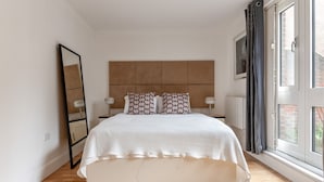 Een slaapkamer met een bed, nachtkastjes, een spiegel en een raam met gordijnen.