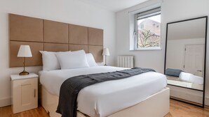 Ein modernes Schlafzimmer mit einem großen Bett, Nachttischen, einem Fenster und einem Spiegel.