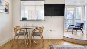 Ein modernes Wohnzimmer mit einem runden Tisch und zwei Stühlen, einem flachbildfernseher an der Wand und einem Balkon mit einem Sessel.