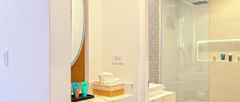 A modern bathroom with a glass shower enclosure, a built-in sink, and a compact refrigerator.