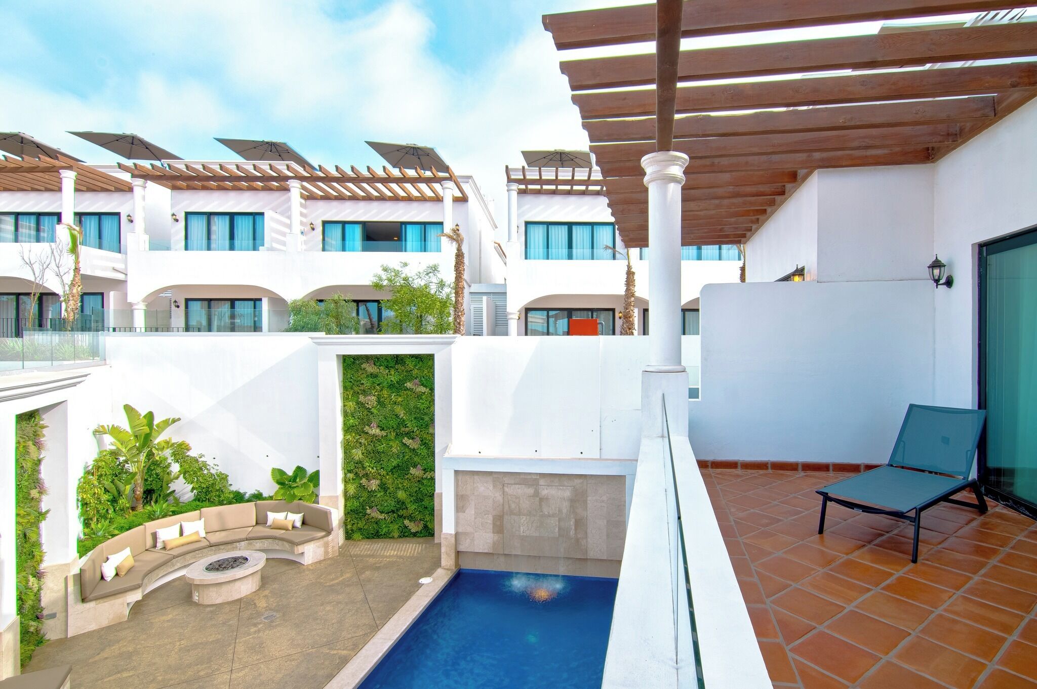 Un hotel moderno con zona de piscina, mobiliario exterior y un porche cubierto.