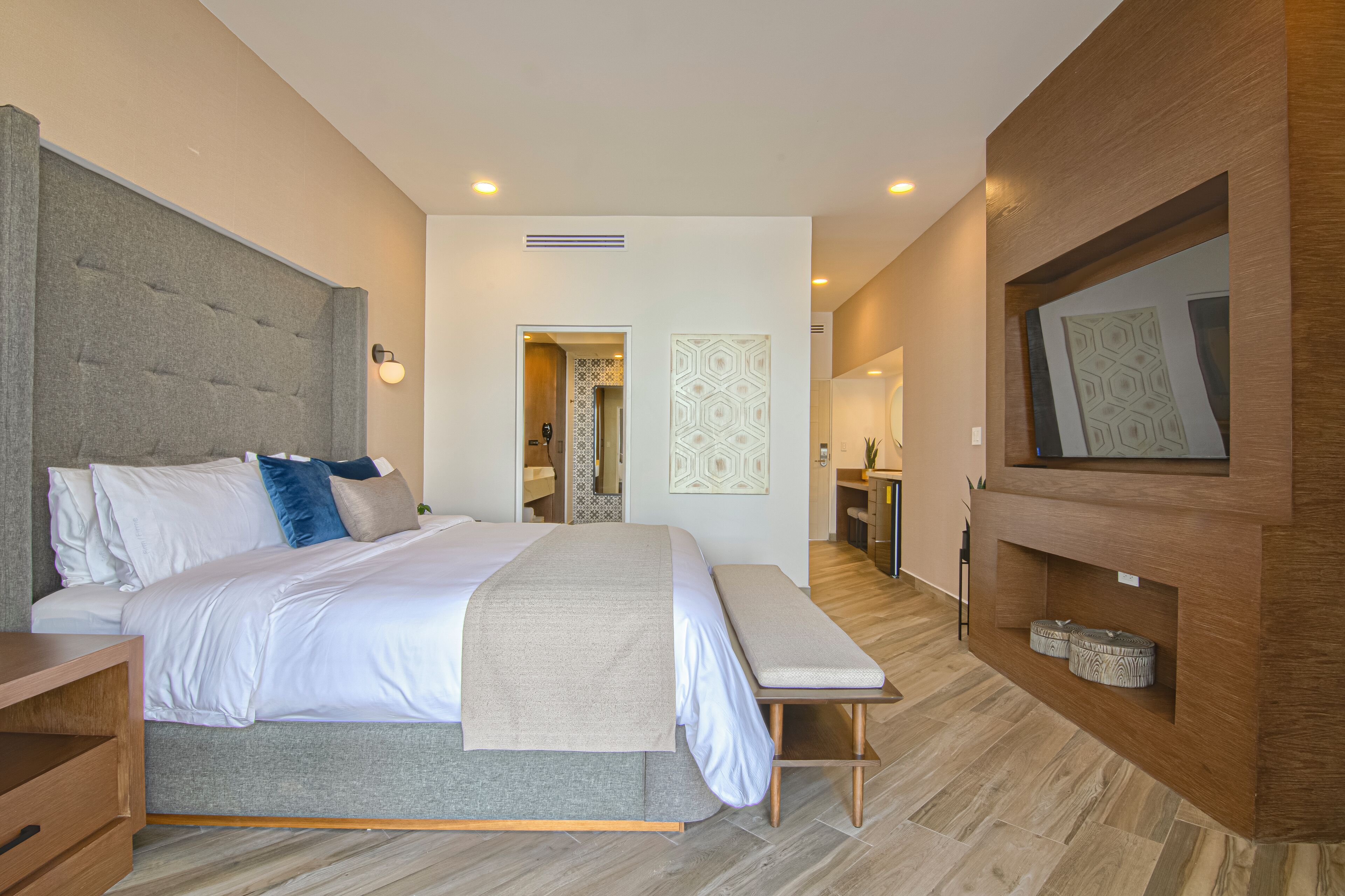 A modern bedroom with a large bed, bedside tables, a bench, a TV, and a wooden panel wall.