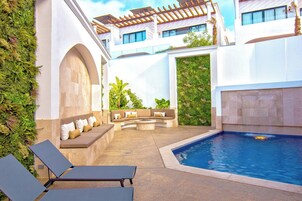 Zona de piscina con área de descanso, pérgola y un muro cubierto de vegetación.