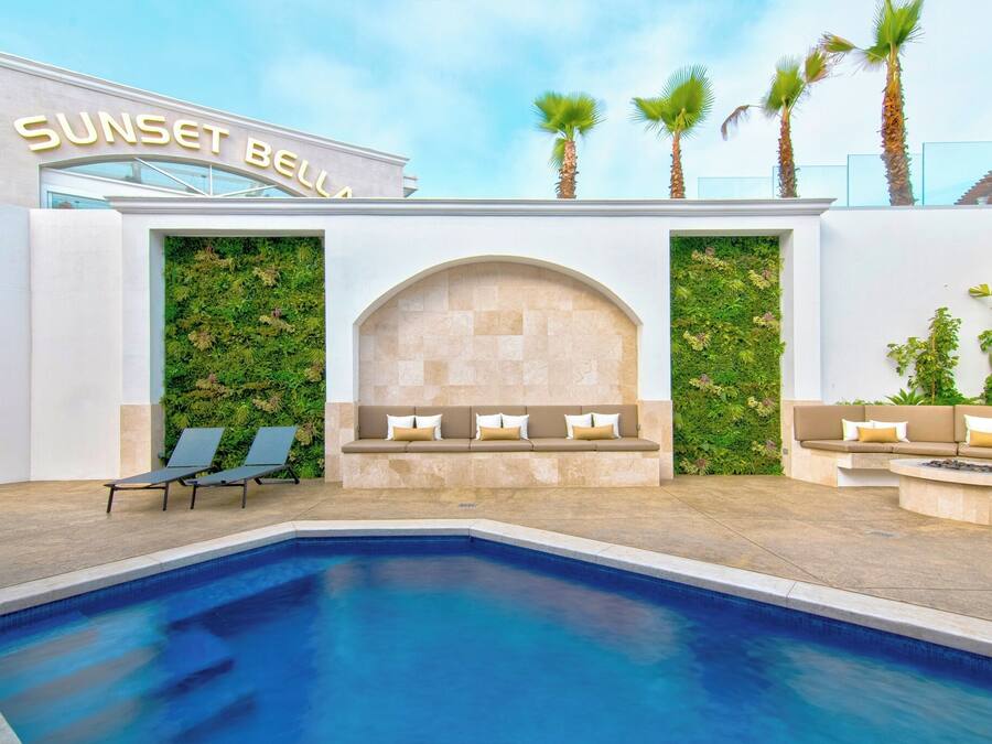 A pool area with lounge chairs, a seating area with cushions, and a wall with greenery.