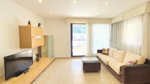 Ein modernes Wohnzimmer mit Flachbildfernseher, einer Couch, einem Couchtisch und einer Glastür, die auf einen Balkon führt.