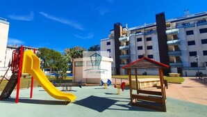 Ein Spielplatz mit einer gelben Rutsche und einer kleinen Holzüberdachung, umgeben von Wohngebäuden.