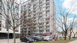 Un edificio residencial de varios pisos con balcones, coches aparcados y cielo despejado.