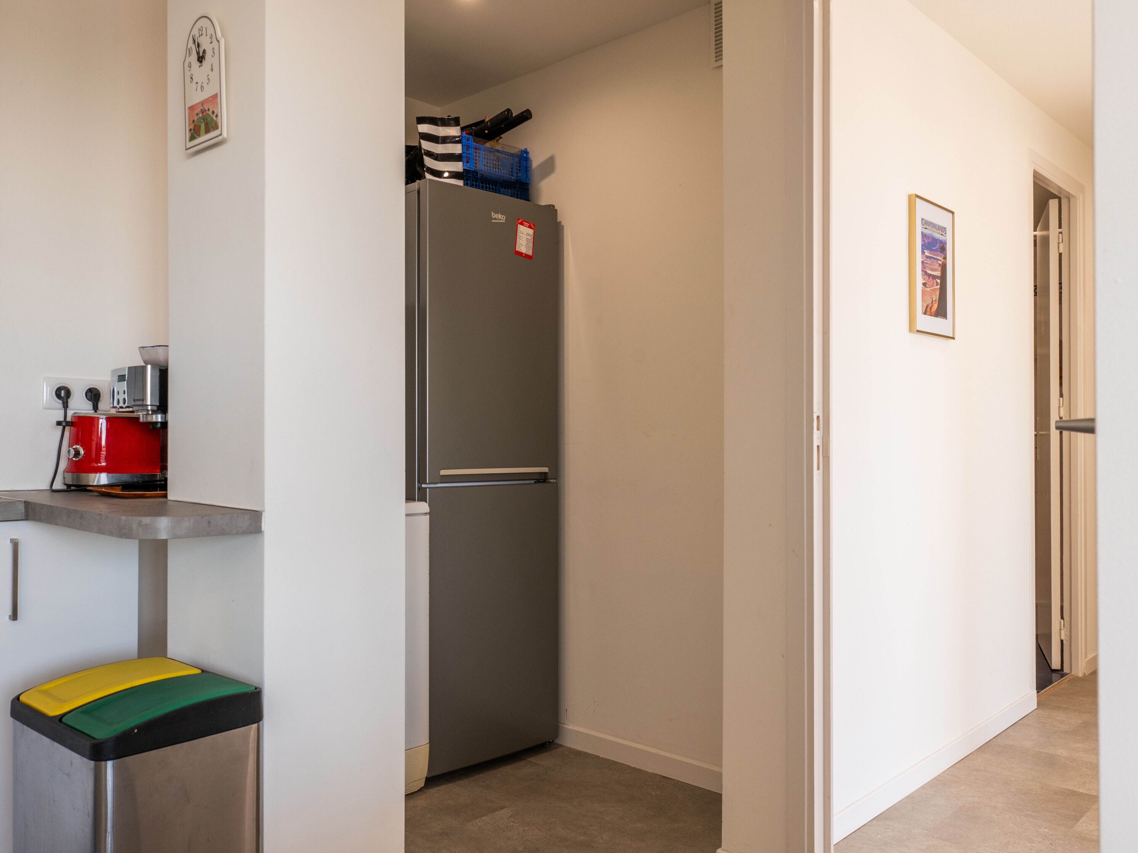 A compact kitchen with a refrigerator, a small trash bin, and a coffee machine.