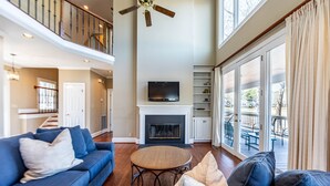 Un salon spacieux doté d’une cheminée, d’un téléviseur fixé au-dessus et d’un balcon aménagé avec du mobilier d’extérieur.