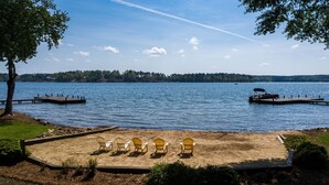 Une vue sur le lac, avec une plage de sable, des chaises en bois, un quai et un bateau.