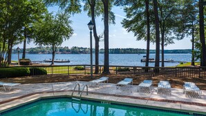 Une piscine avec vue sur un lac et un quai, entourée d’arbres et de chaises longues.