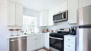 A modern kitchen with white cabinets, stainless steel appliances, and a window providing natural light.