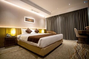 A hotel room with a large bed, bedside lamps, a desk, and a view of the cityscape through the window. - Pearl Hotel (Dhaka)