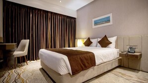 A hotel room with a large bed, a bedside table with a lamp, a chair, and a view of the city through the window. - Pearl Hotel (Dhaka)