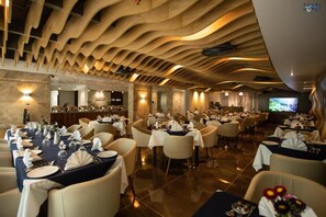 A spacious restaurant with multiple dining tables set for guests, a modern ceiling design, and a television screen in the background. - Pearl Hotel (Dhaka)