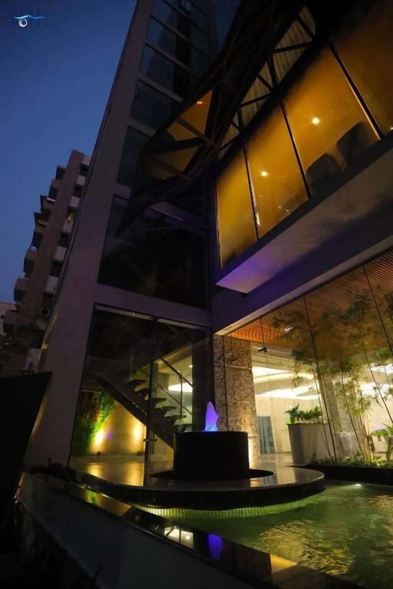 A modern building with a glass facade, a pool area with a water feature, and a well-lit interior.