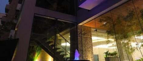A modern building with a glass facade, a pool area with a water feature, and a well-lit interior.
