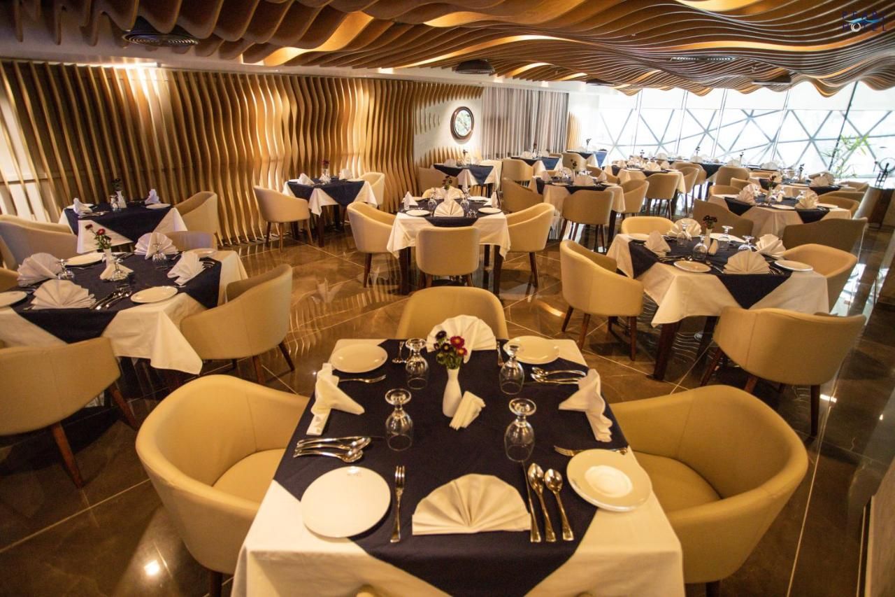 A restaurant with round tables set for dining, featuring a modern interior with a unique ceiling design and a large window in the background.