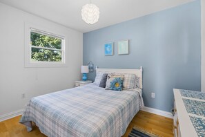 A bedroom with a bed, a nightstand, a lamp, and a window.