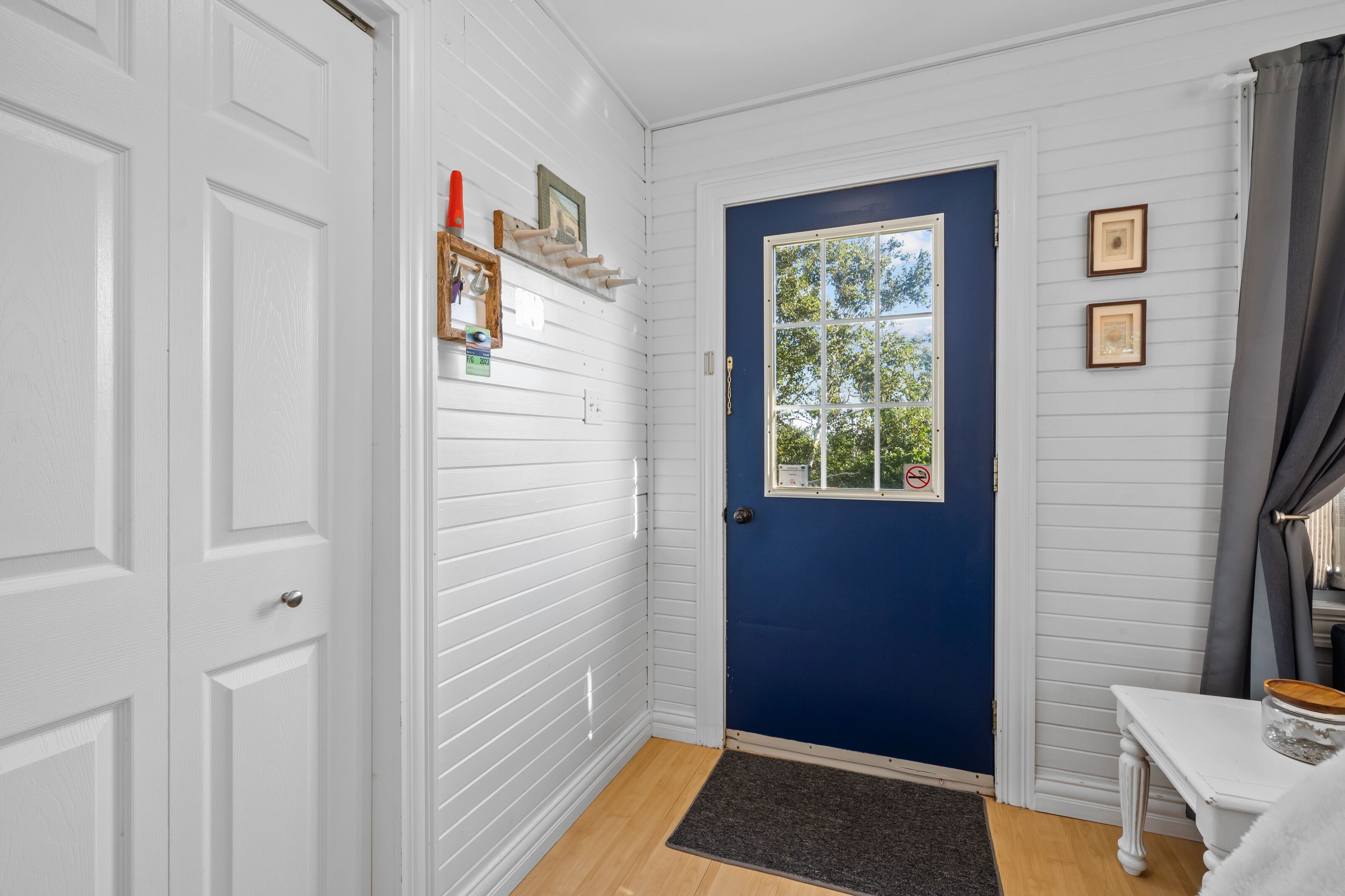 Una habitación con puerta azul, paredes blancas, una ventana pequeña y suelo de madera.