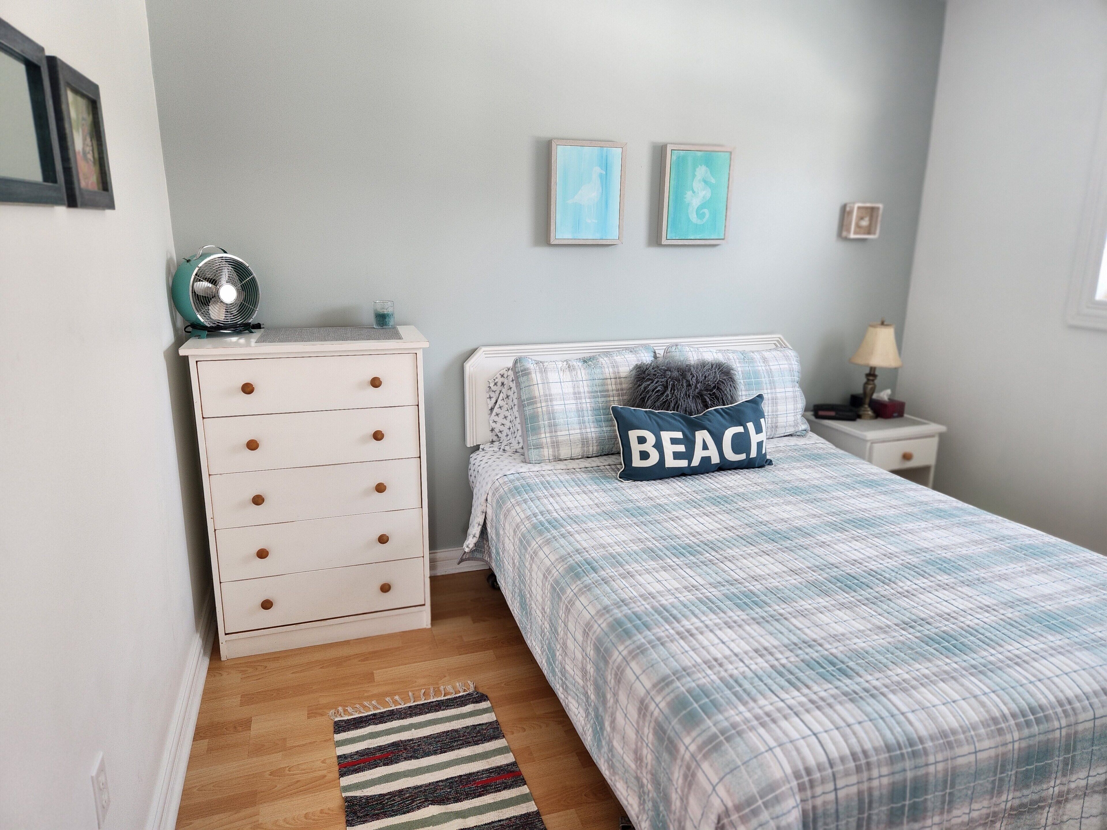 Ein Schlafzimmer mit Bett, Kommode, Nachttisch, Lampe und zwei Wandbildern.