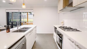 Uma cozinha moderna com armários brancos, lava-louças Bosch, fogão a gás e iluminação pendente.