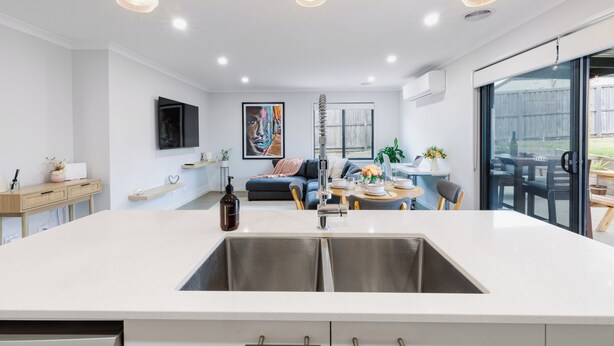 Uma cozinha moderna com uma ilha central, uma sala de jantar com mesa e cadeiras, e uma sala de estar com sofá e obras de arte.