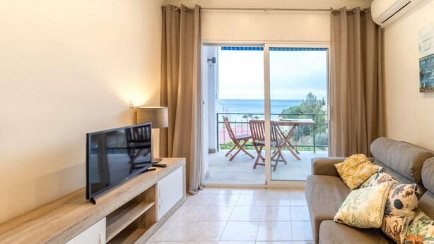 A living room with a TV, a sofa, a balcony with a table and chairs, and a view of the sea. - Les Tonyines 67 - Apartment with views and terrace (Llança)