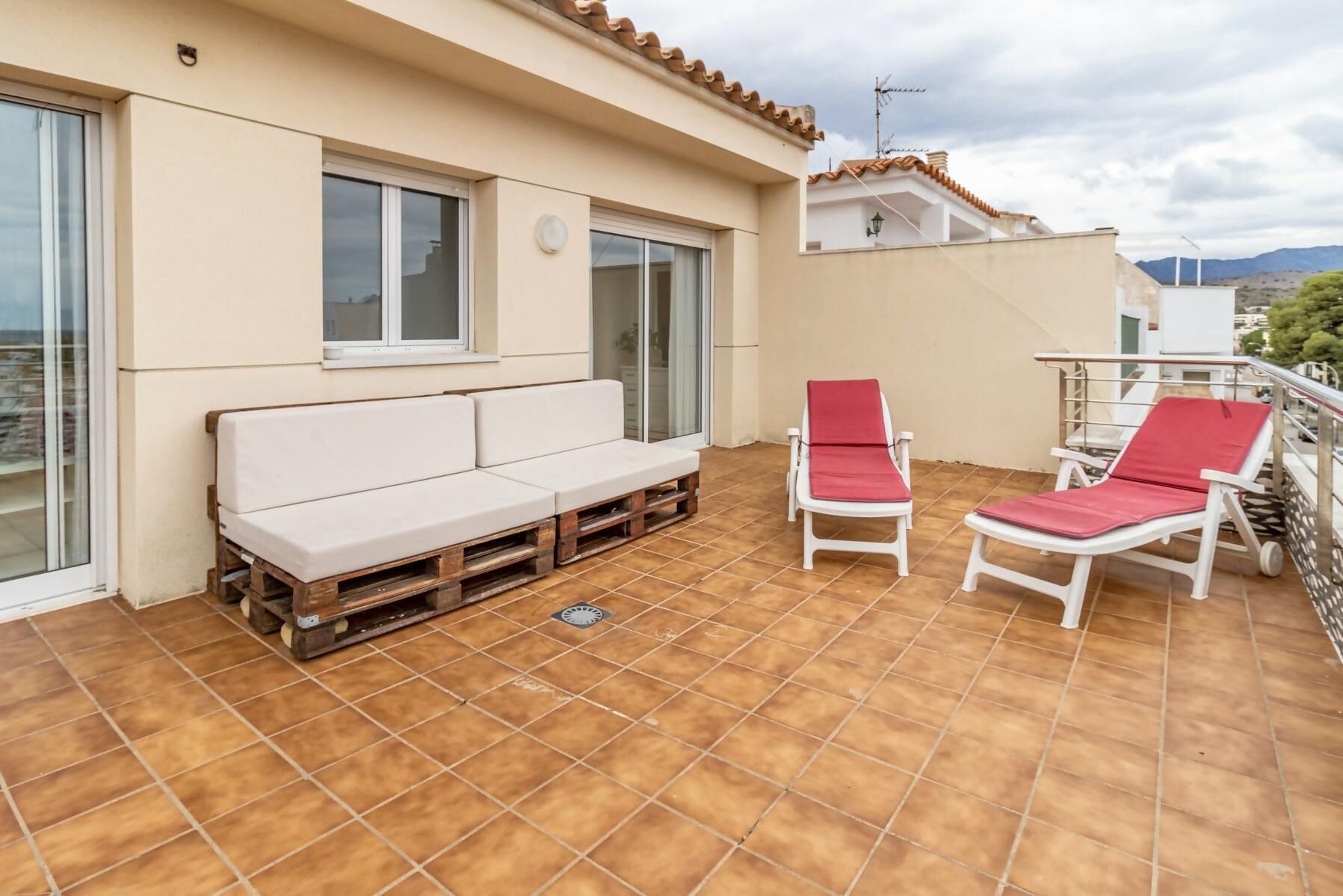 Un balcon avec un canapé blanc, deux fauteuils rouges et un sol carrelé.