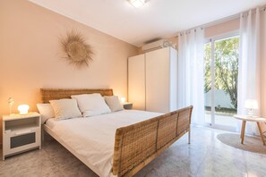 A bedroom with a bed, nightstands, a lamp, a wicker headboard, a wall decoration, and a view through a glass door.