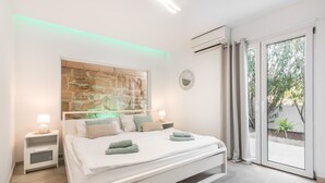 Ein modernes Schlafzimmer mit einem großen Bett, zwei Nachttischen, einer Wand-Klimaanlage und einer Glastür zum Außenbereich.