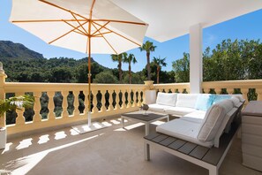 A balcony with a white sofa, a wooden table, and an umbrella.