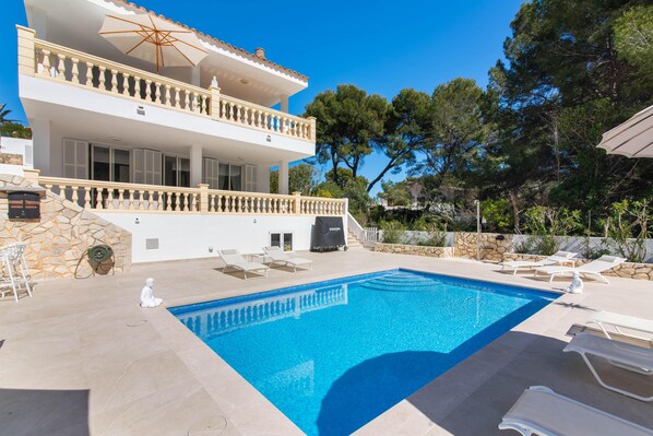 A two-story building with a swimming pool, outdoor seating, and a stone wall.