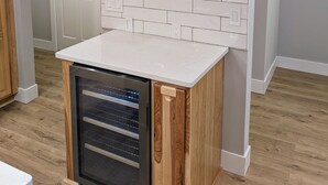 Une cuisine dotée d’un four encastré, d’un plan de travail blanc recouvert de carreaux, d’étagères en bois ornées d’objets décoratifs et d’un comptoir blanc.