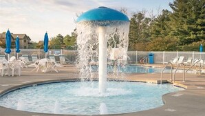 Une piscine agrémentée d’une fontaine, entourée de chaises longues et de parasols.