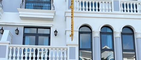 Un edificio de varios pisos con fachada blanca, balcones con barandillas negras y una cafetería en la planta baja.