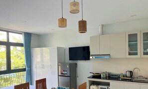 A modern kitchen with a refrigerator, stove, and microwave. There is a dining area with a table and chairs. -  Ngan Ha Star Homestay - Grand World Phu Quoc (Phu Quoc)
