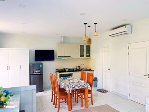 A compact kitchen with a dining area, a TV mounted above the counter, and a white door on the right.