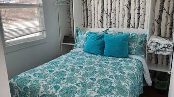 A bedroom with a bed, a window with blinds, a wardrobe, and a wall with a tree pattern.