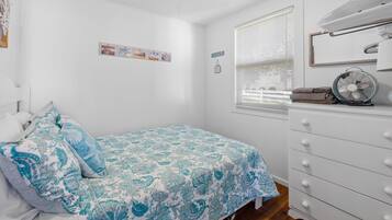Une chambre à coucher avec un lit, une commode, un ventilateur et une fenêtre avec des stores.