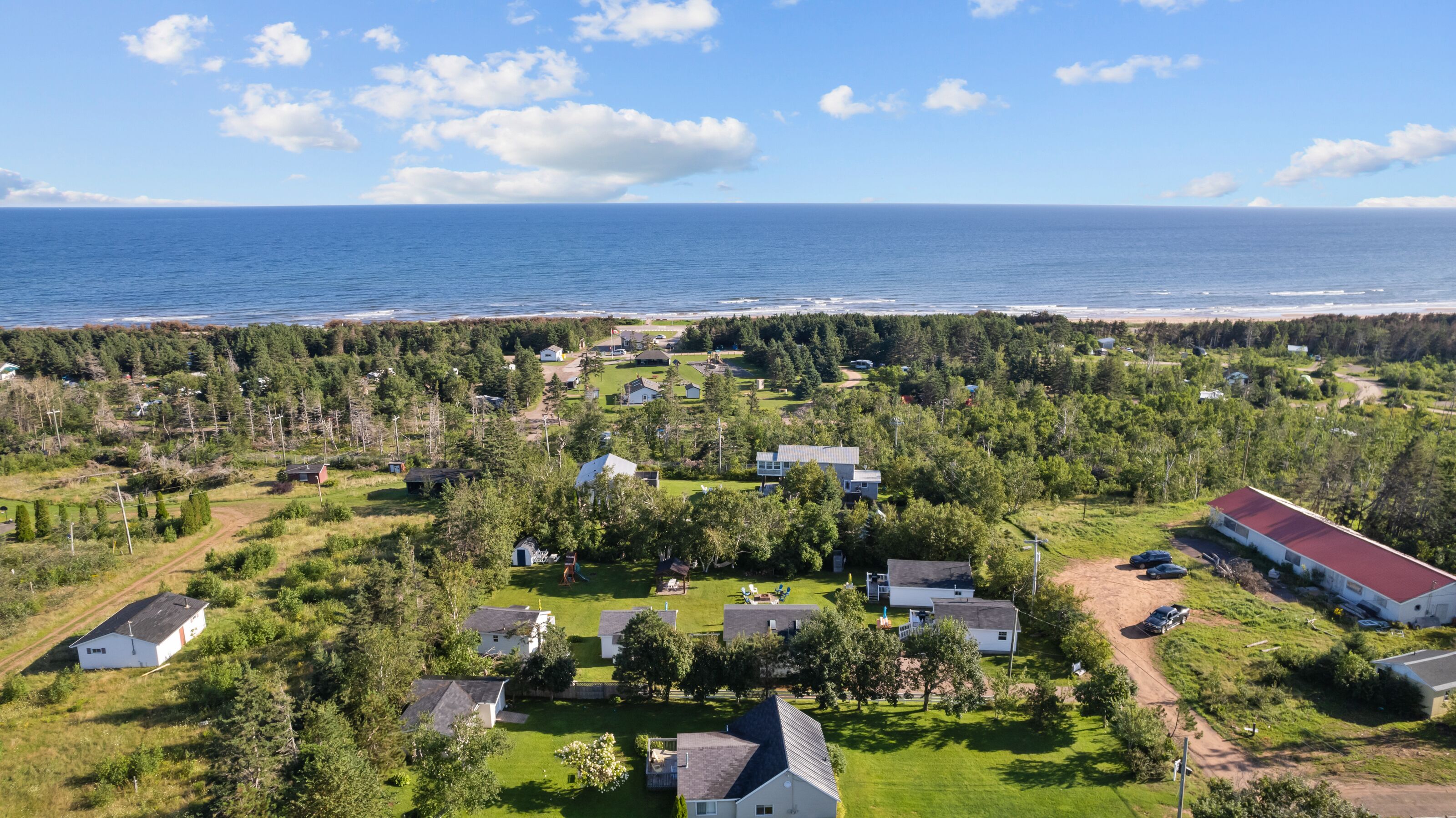 Vue aérienne d’un quartier résidentiel situé sur la côte, avec des maisons, des espaces verts et une plage en arrière-plan.