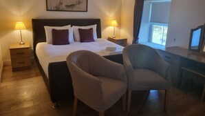 A hotel room with a bed, two bedside tables with lamps, a desk with a chair, and a window with curtains. - Auchendennan Farm Cottage - sleeps 6 guests  in 3 bedrooms (Alexandria)