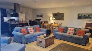 A modern living room with two sofas, a coffee table, and a dining area with a table and chairs. - Auchendennan Farm Cottage - sleeps 6 guests  in 3 bedrooms (Alexandria)